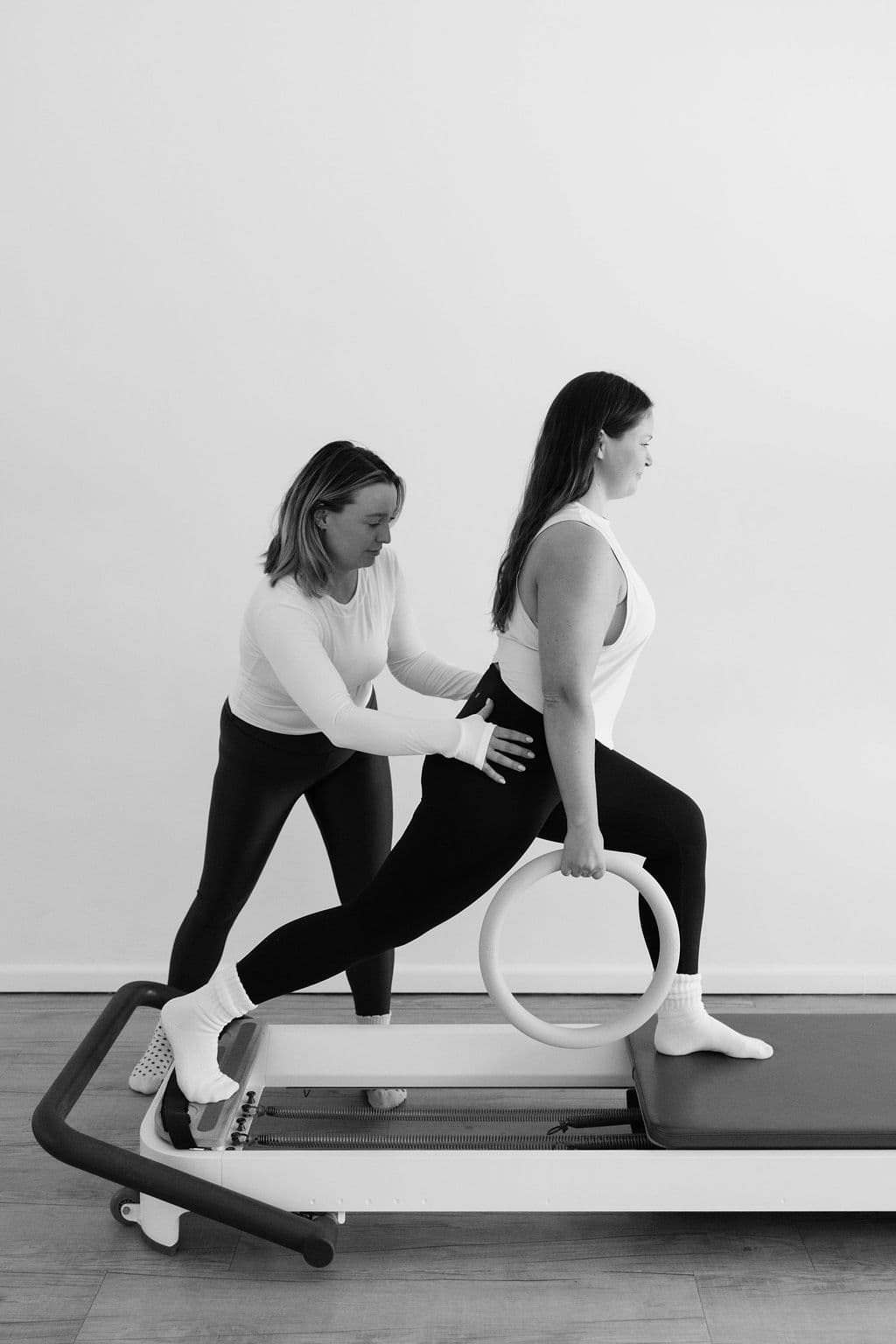Instructor assists a woman performing a Pilates reformer lunge with a magic circle.